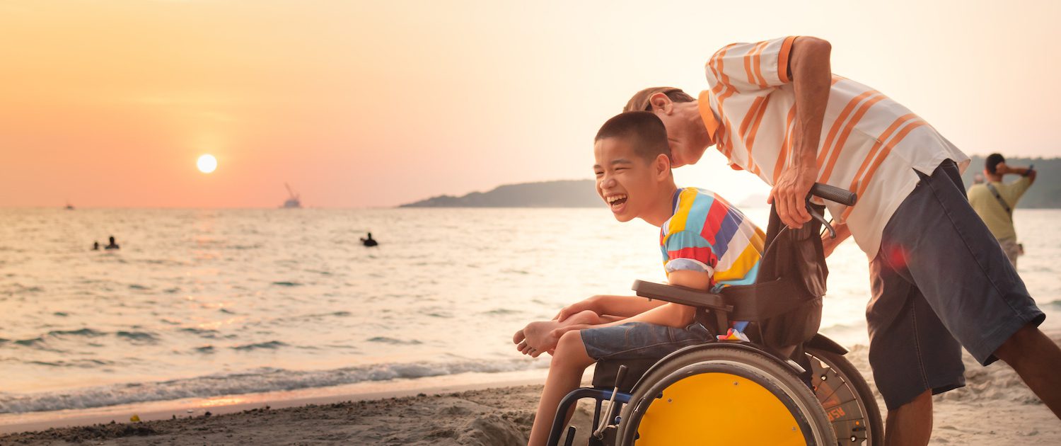 Courage Support Services Hero IMG 1 - Asian special child on wheelchair is happily on the beach with father