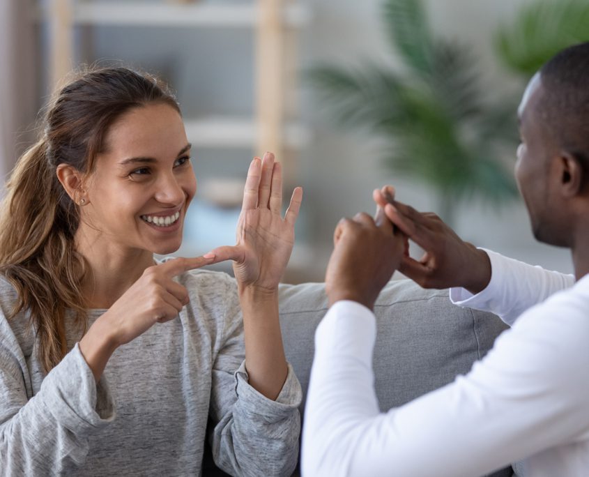 Why So Many People Choose Courage Support Services - Smiling mixed ethnicity couple or interracial friends talking with sign finger hand language